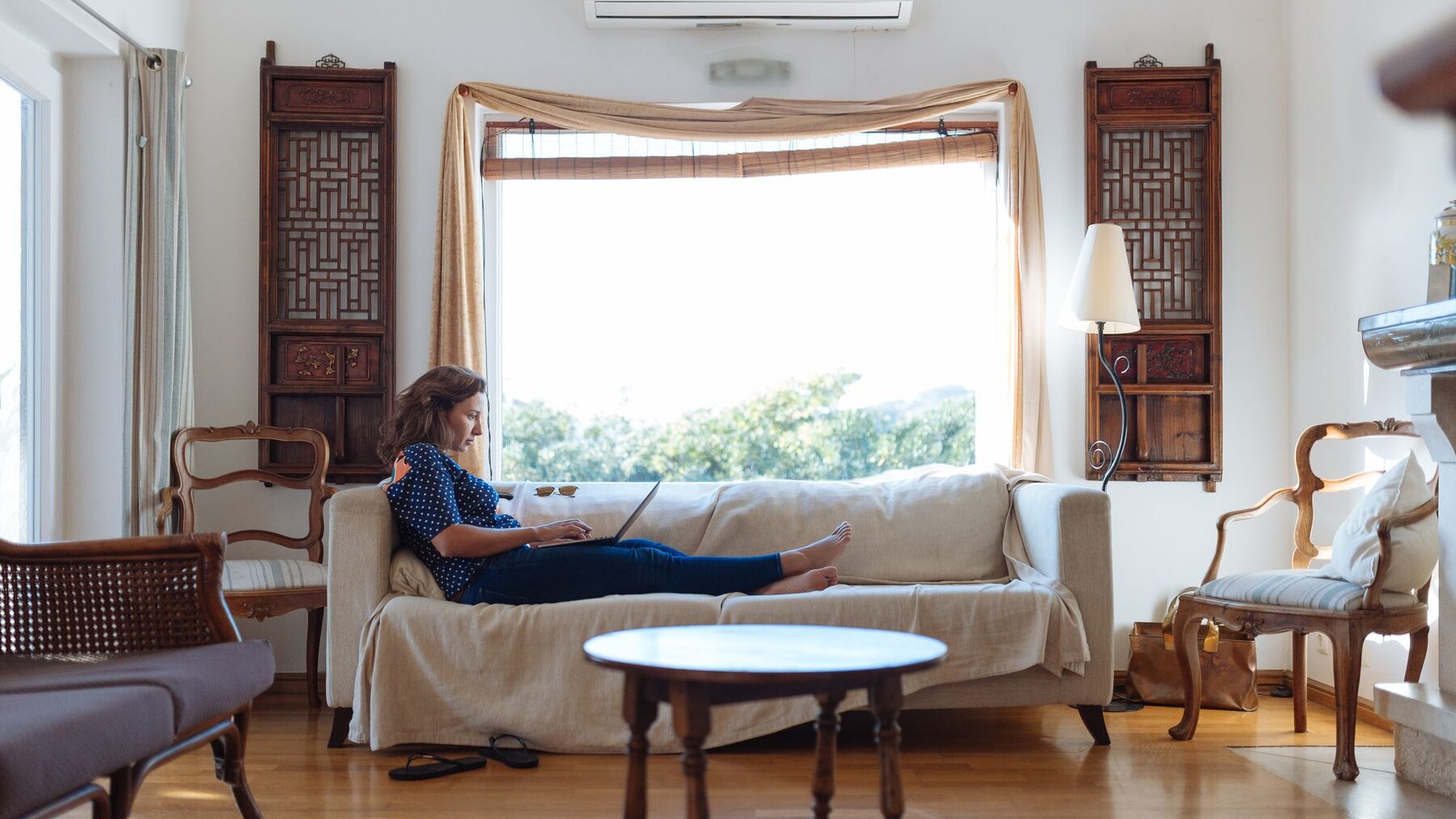 Stanislava Giosheva working on a design at home, seated on a sofa in a sunlit living room