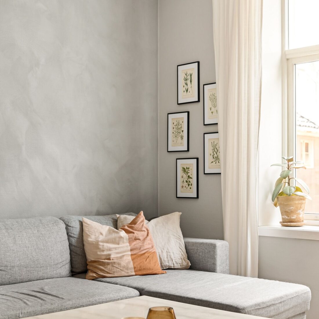 Living room with a grey sofa, framed gallery wall and soft daylight from a tall window