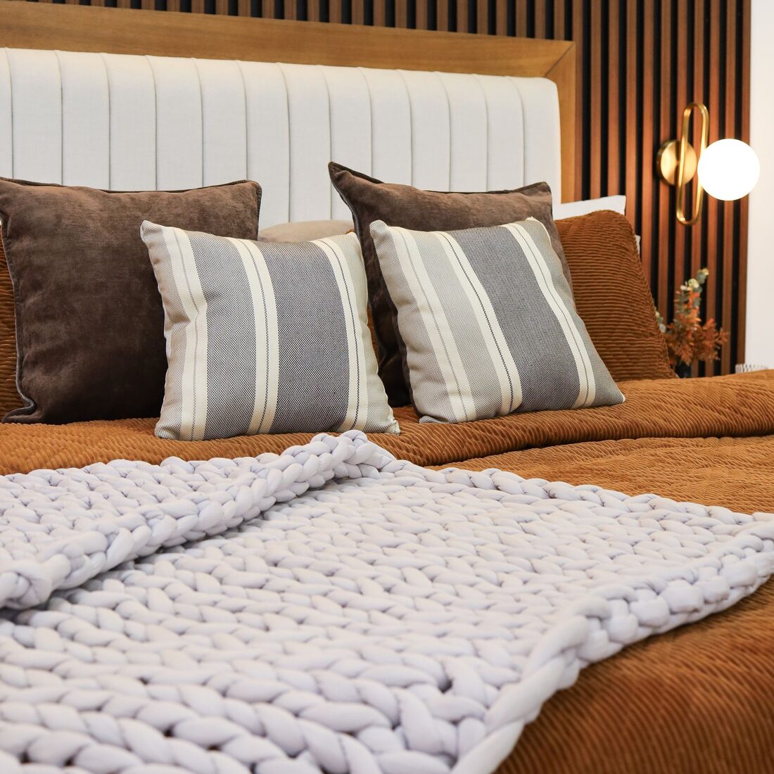 Bedroom with a slatted timber headboard wall, rust bedding and a chunky knit throw
