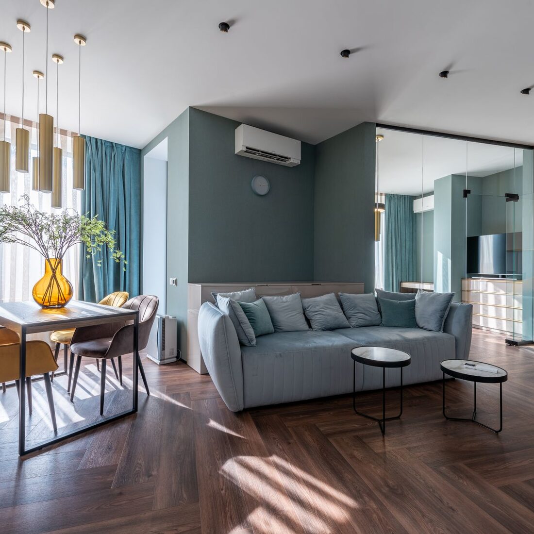 Open-plan living and dining room with a deep green wall and herringbone parquet floor