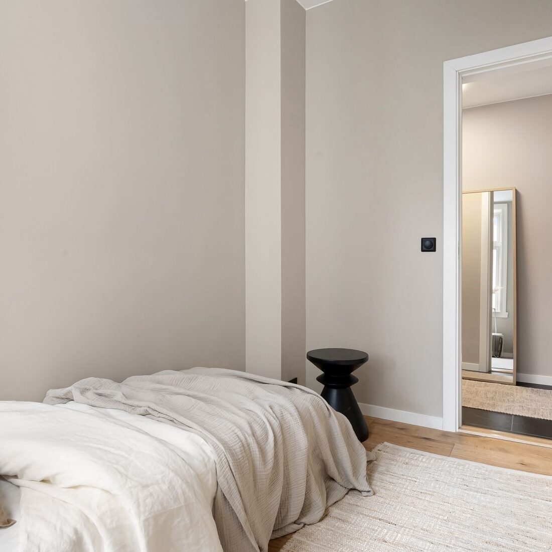 Minimal bedroom in warm off-white with linen bedding and a small black bedside table
