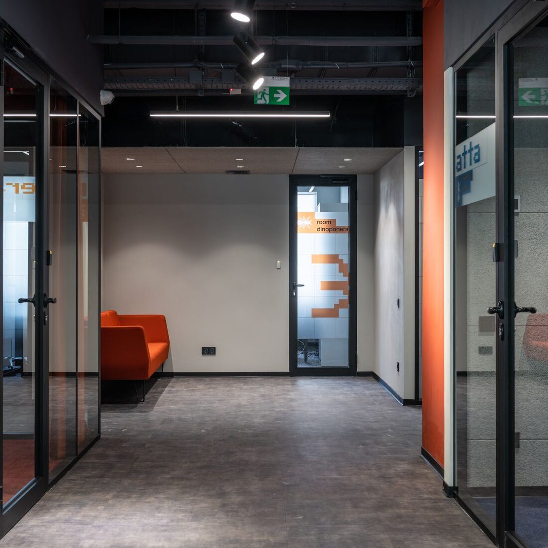 Office corridor with glass partitions and a bright orange lounge sofa