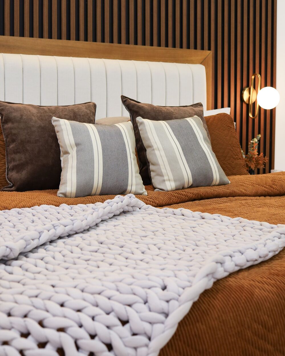 Bedroom with a slatted timber headboard wall, rust bedding and a chunky knit throw