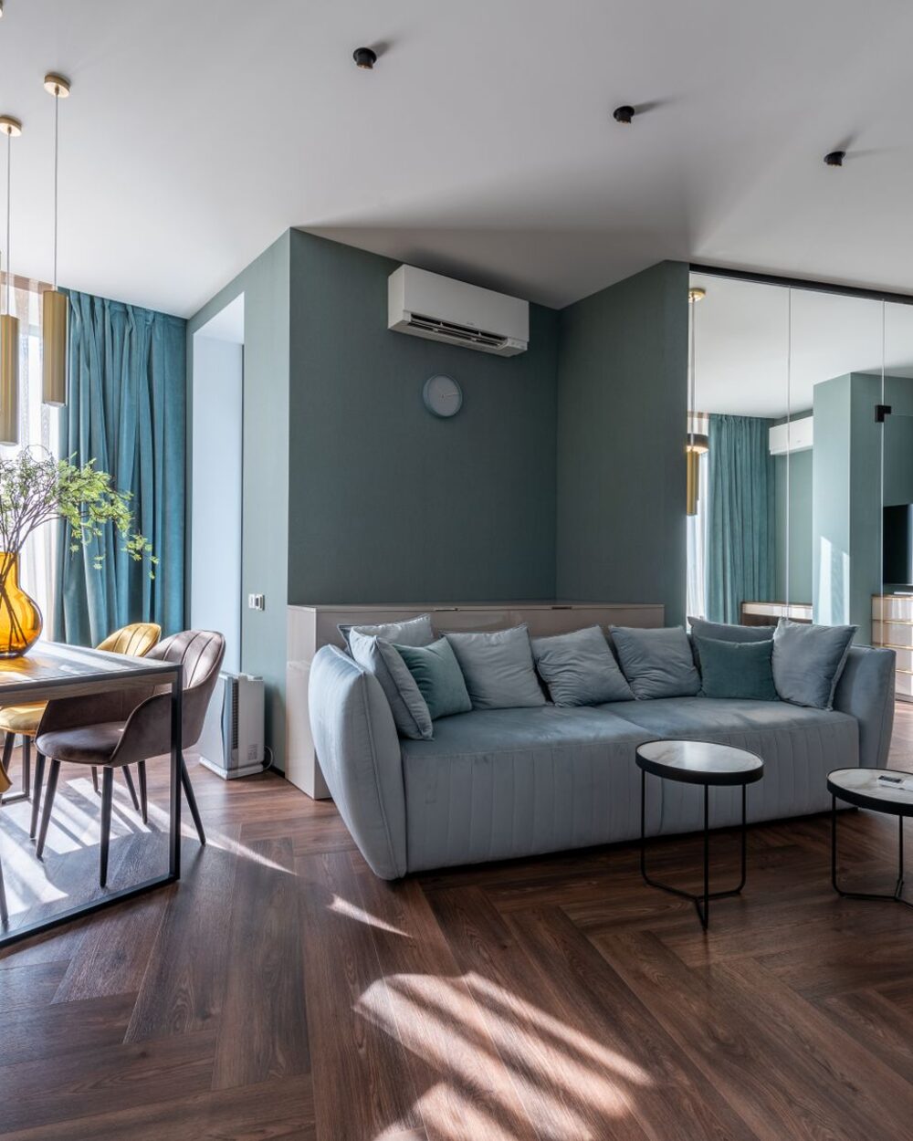 Open-plan living and dining room with a deep green wall and herringbone parquet floor