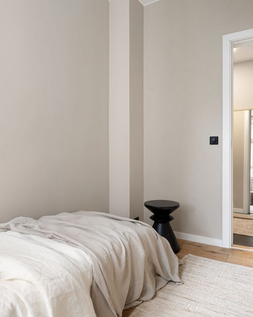 Minimal bedroom in warm off-white with linen bedding and a small black bedside table
